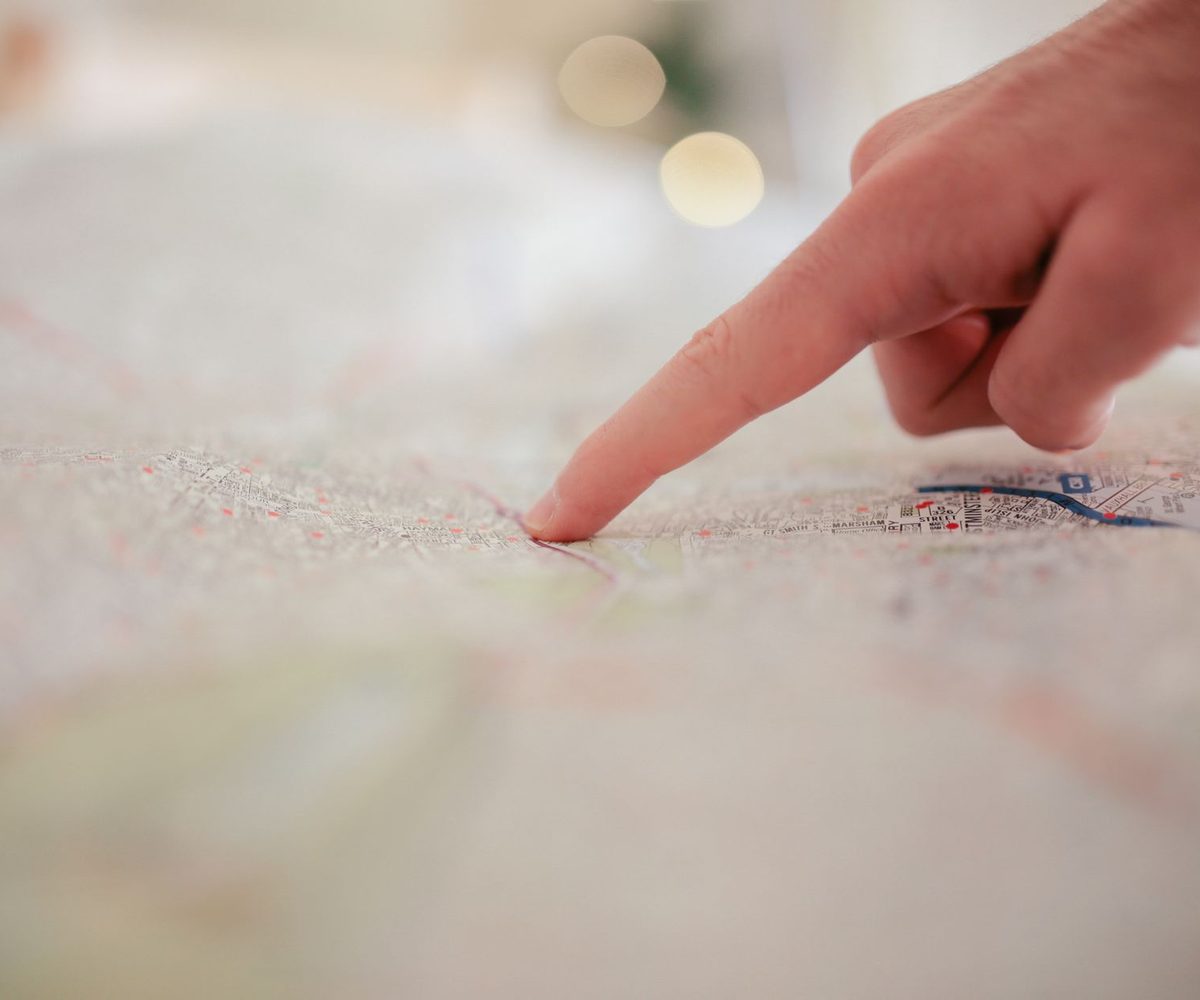 A finger pinpointing a single location on a detailed street map, the problem compliance geocoding solves