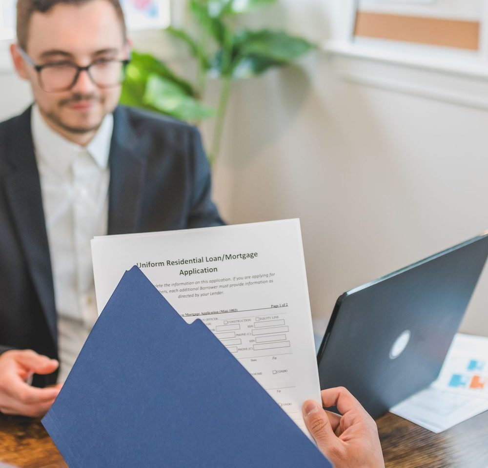 Loan officer holding a Uniform Residential Loan/Mortgage Application, the source record behind a HMDA LAR entry